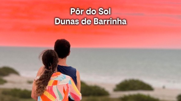 Casal admirando o pôr do sol nas Dunas de Barrinha, com céu laranja ao fundo.